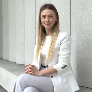 Paulina Stępniewska w białym żakiecie siedzi na ławce. Paulina jest profesjonalną i przyjazną ekspertką kredytową, zawsze dostępną dla swoich klientów.