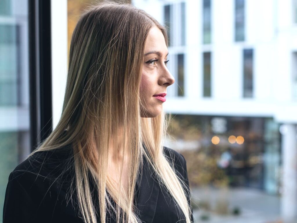 Paulina Stępniewska spogląda przez okno swojego biura na miasto. Zdjęcie jest symbolem refleksji, odpowiedzialności i długoterminowego podejścia w swojej pracy jako ekspertka finansowa specjalizująca się w kredytach hipotecznych.