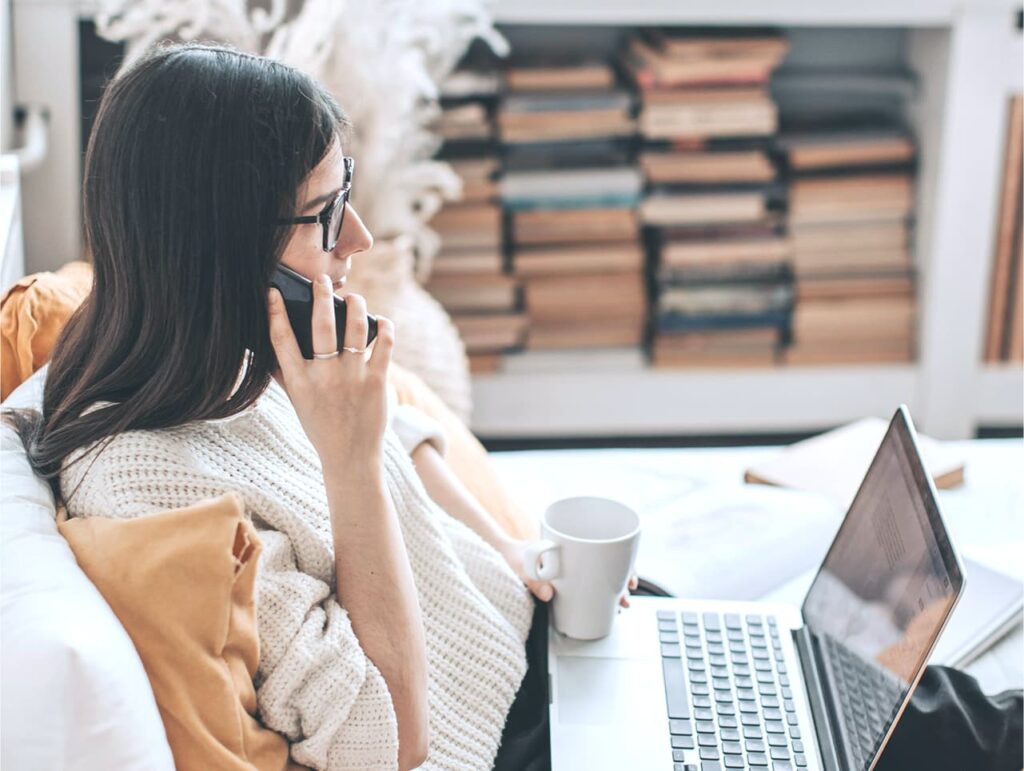 Kobieta rozmawia przez telefon, pracując na laptopie.